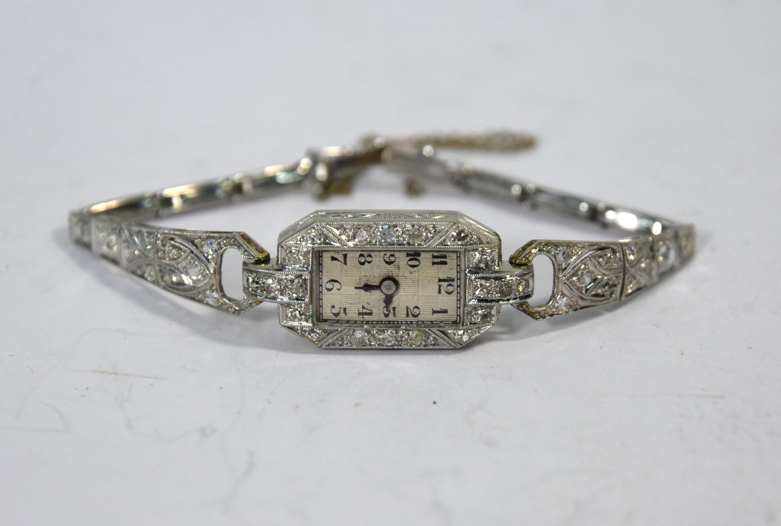 Lady's Art Deco platinum and diamond cocktail watch: A lady's Art Deco platinum and diamond cocktail watch with silvered checquered rectangular dial, on hinged bracelet, 13g net of movement