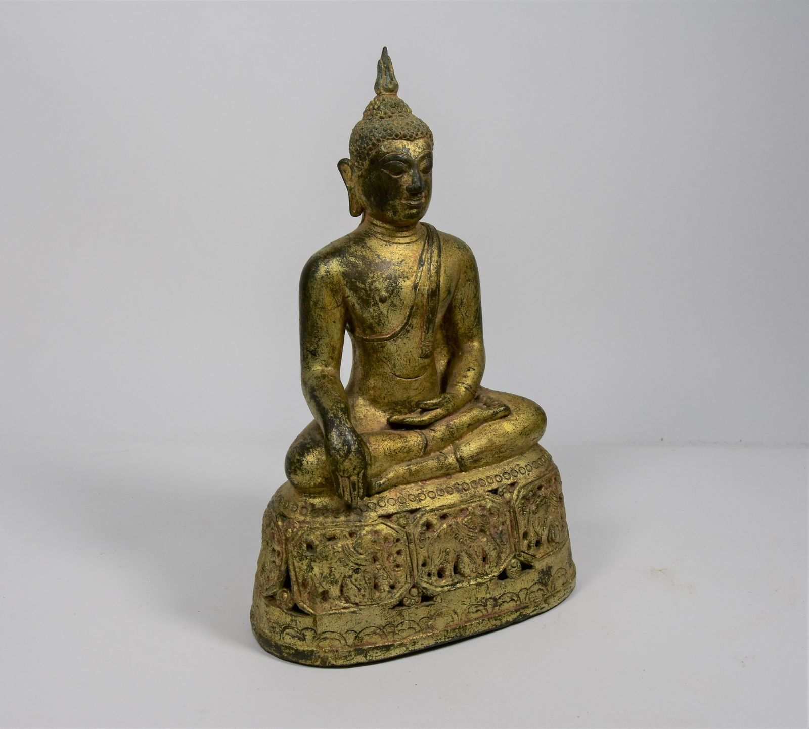 A 19th century Burmese gilt bronze figure of buddha: A 19th century Burmese gilt bronze figure of buddha wearing loose robes, seated with hands in bhumisparsha mudra on a reticulated elephant cast base, 25.5 cm high