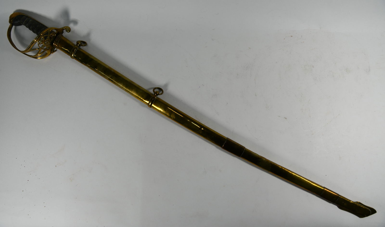 A Victorian cavalry sabre: A Victorian cavalry sabre, 80 cm slightly curved blade with full-length back-rib, pierced brass basket hilt with wired fishskin grip, hinged retention clip a/f, in associated contemporary brass scabba