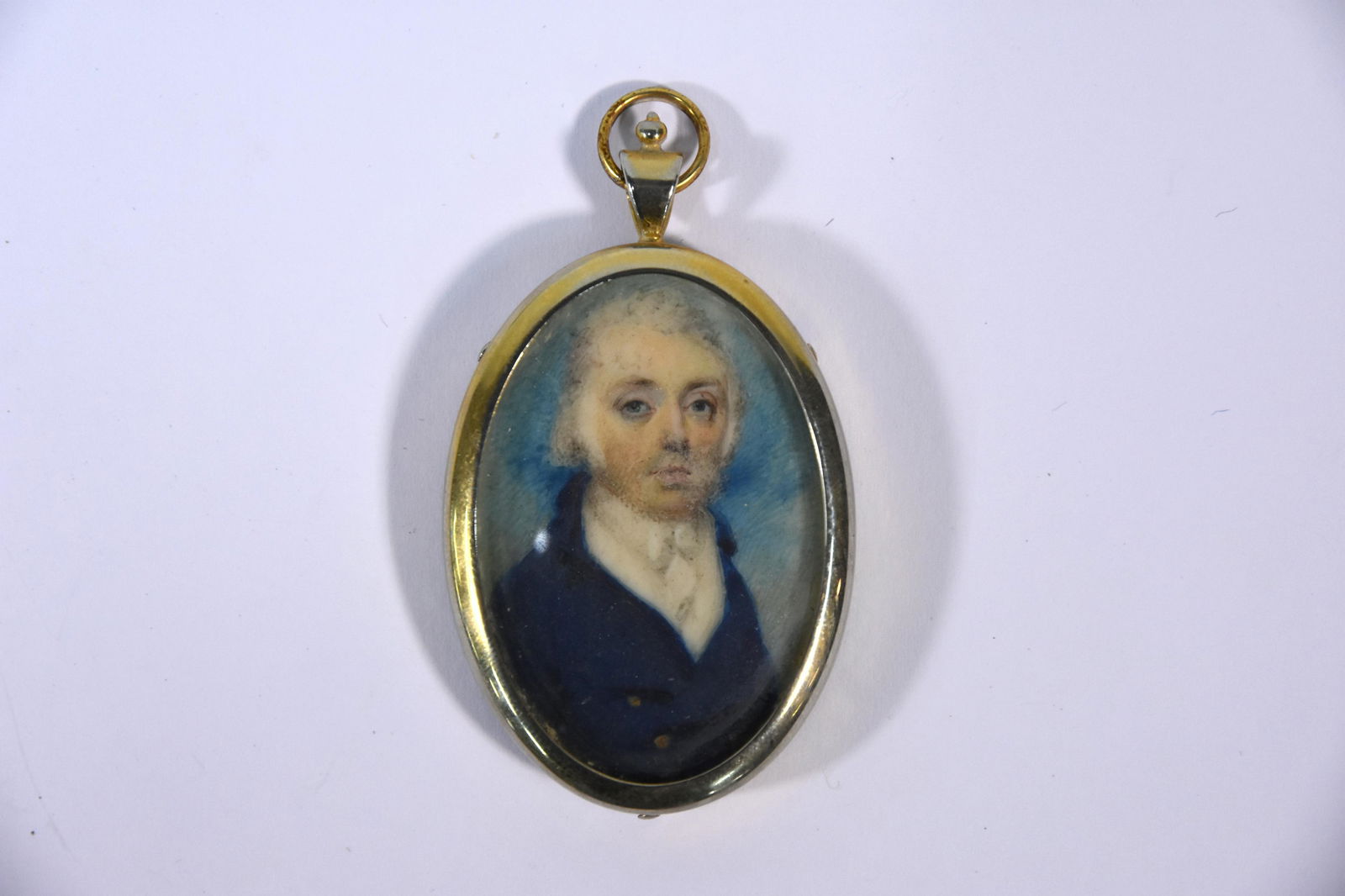 A small George III oval portrait miniature on ivory of: A small George III oval portrait miniature on ivory of a gentleman, John Ward Stratton, in powdered wig and blue coat, unsigned, 4.5 x 3 cm, in brass pendant frame