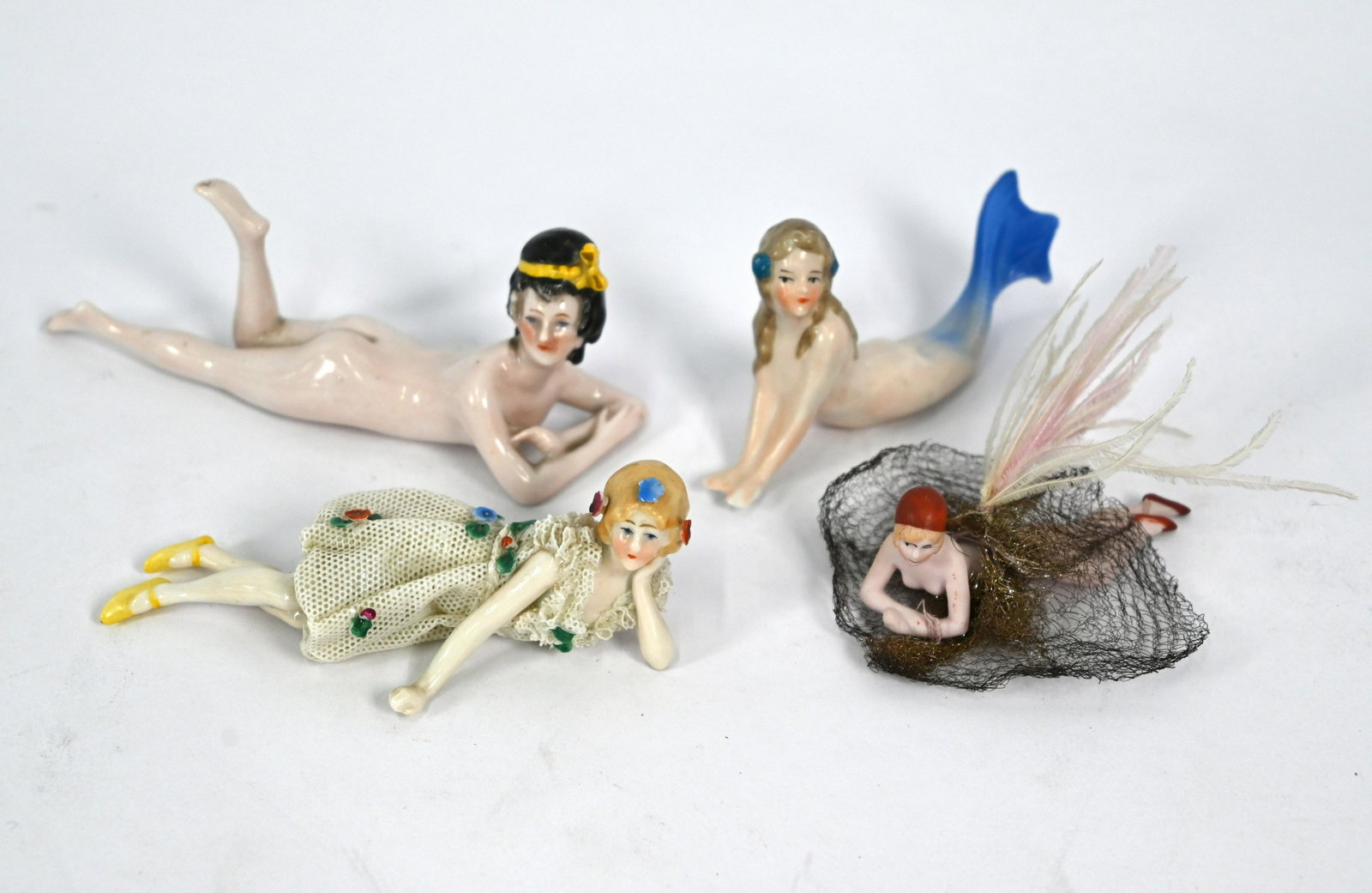 A Continental ceramic small reclining female nude: A Continental ceramic small reclining female nude, 13.5 cm high to/w a similar mermaid, miniature bisque 'bathing beauty' and a reclining girl in lacy dress (4) Buyers premium 30% (inc VAT)