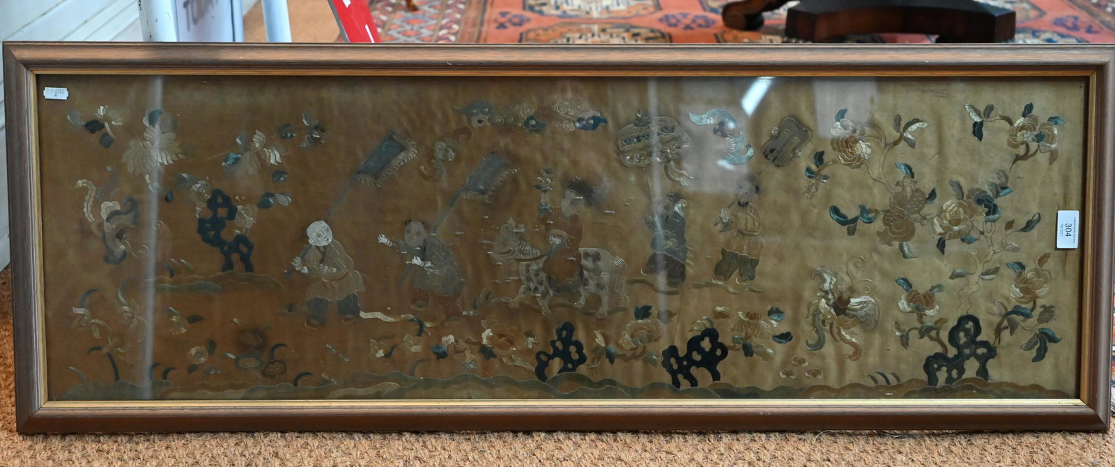 A Chinese silk embroidered panel depicting children,: A late 19th century Chinese Kesi work panel embroidered in coloured threads depicting a procession of children amongst butterflies, bats and flowers, one riding a mythical beast against faded gold gro