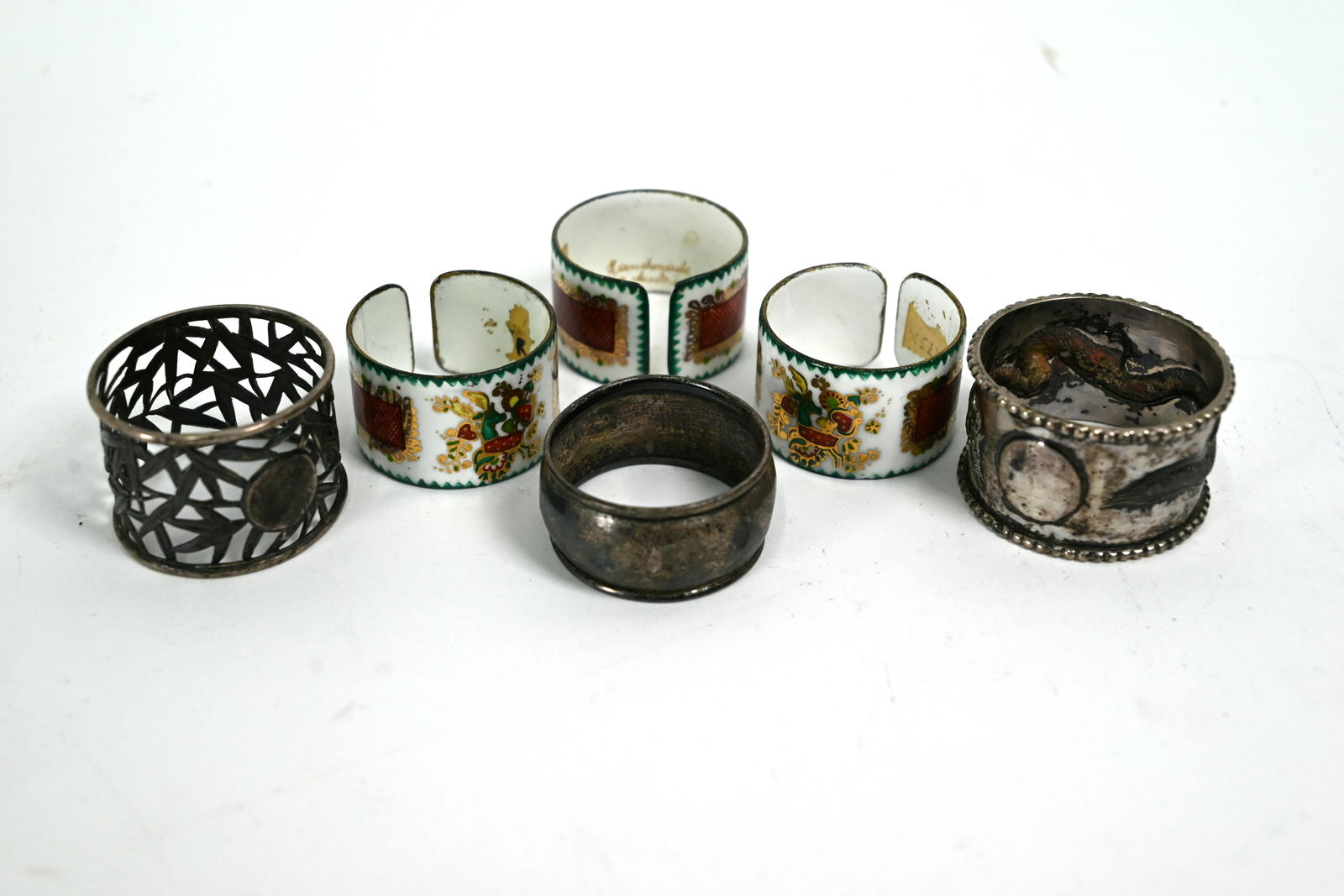 Six various napkin rings: A Chinese white metal napkin ring, embossed and chased with a dragon, another napkin ring with pieced bamboo design, a .925 standard napkin ring and three Austrian enamelled napkin rings (6)