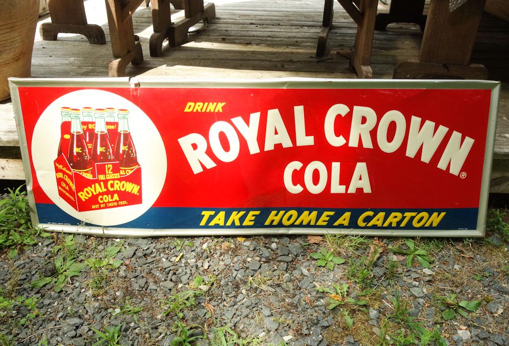 Royal Crown Cola Metal Advertising Sign: A vintage advertisement for Royal Crown Cola featuring a six-pack of bottles and the phrase "Take Home A Carton" depth is on turned edges top and bottom 53.75" x 18" x0.75"