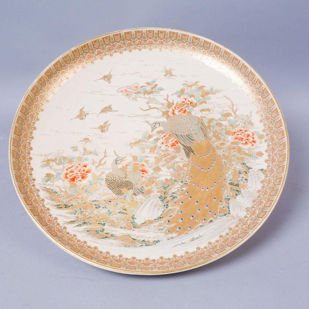 Signed Satsuma Meiji Japan Gilded Peacock Charger 18": Signed Satsuma charger. This fine piece features a peacock and peahen rendered in gilded and enamel paints. Smaller birds fly overhead on the off-white porcelain, broken up by wispy gilded clouds. The