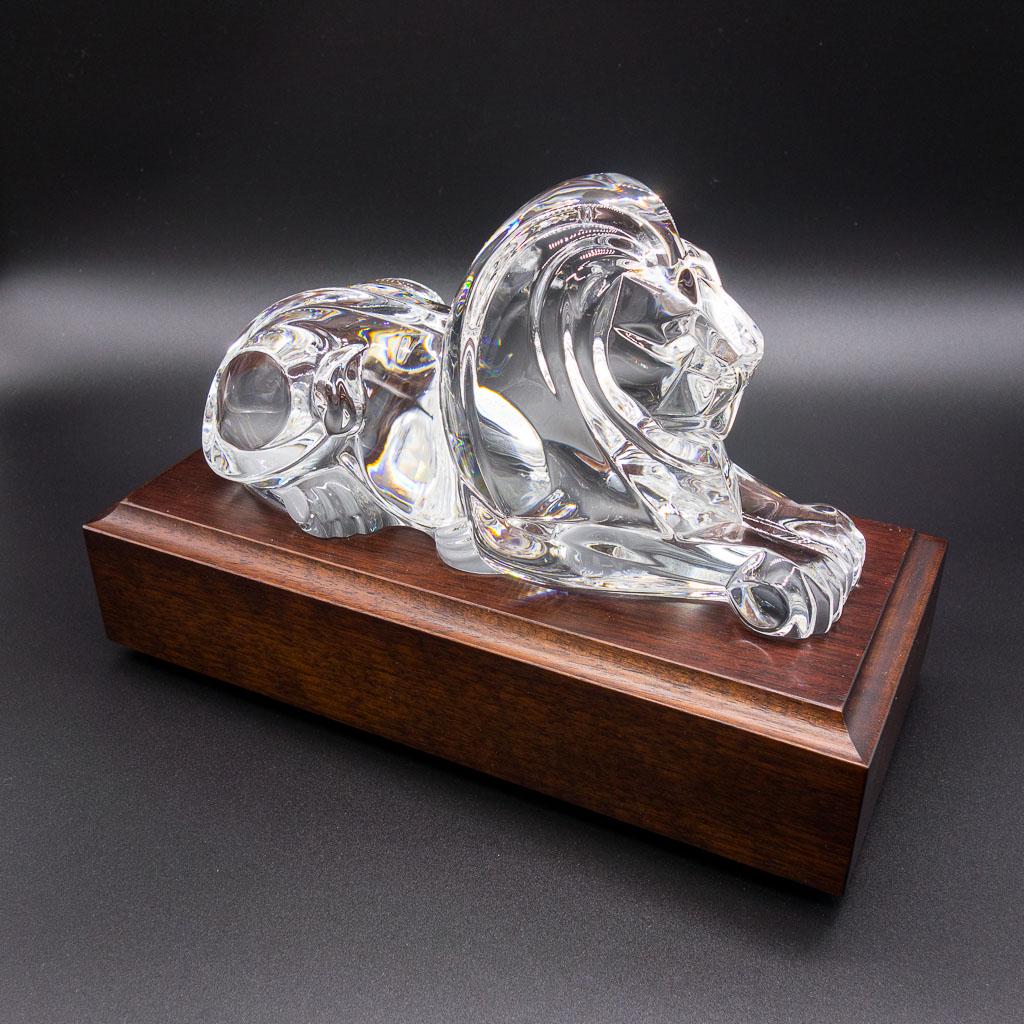 Signed Steuben Lion Crystal Figurine w Walnut Base: Regal and commanding even in repose, the powerful lion guards his domain. A dignified tribute in crystal for a respected executive. Includes walnut base. Design by Lloyd Atkins in 1986. Signed "Steube