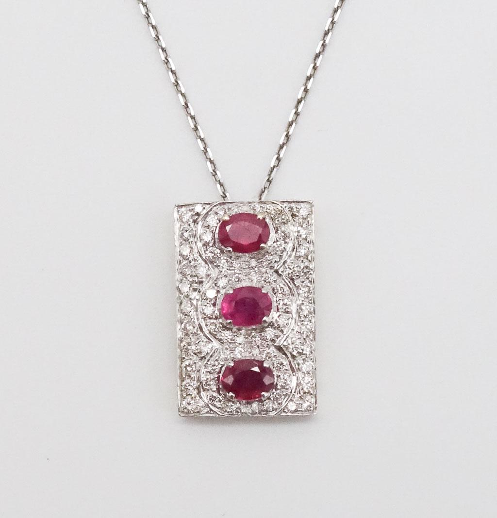 18K White Gold Diamond Ruby Pendant Necklace: 18K white gold rectangular ruby and diamond pendant on a sterling silver chain that also features oval rubies and round bead set diamonds. The rectangular pendant hangs on a 18" silver chain. This pen