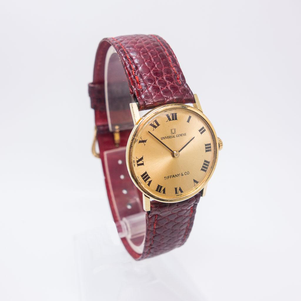 Tiffany Swiss Universal Geneve 14K Gold Wristwatch: This vintage Tiffany & Co. Swiss Universal Geneve ladies wristwatch is rendered in 14K yellow gold. The slim watch case frames a gold tone dial with Roman Numeral indices. This watch is 8.75", the dia