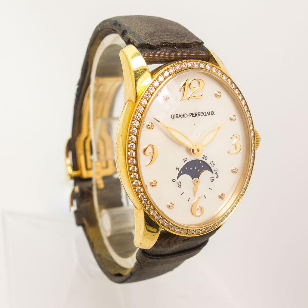 Girard Perregaux Cat's Eye Moonphase Automatic Watch: This lady's Girard Perregaux Cat's Eye moonphase automatic watch features an 18K yellow gold oval case with exhibition back, a diamond bezel, a diamond Arabic mother of pearl dial, and a brown metalli