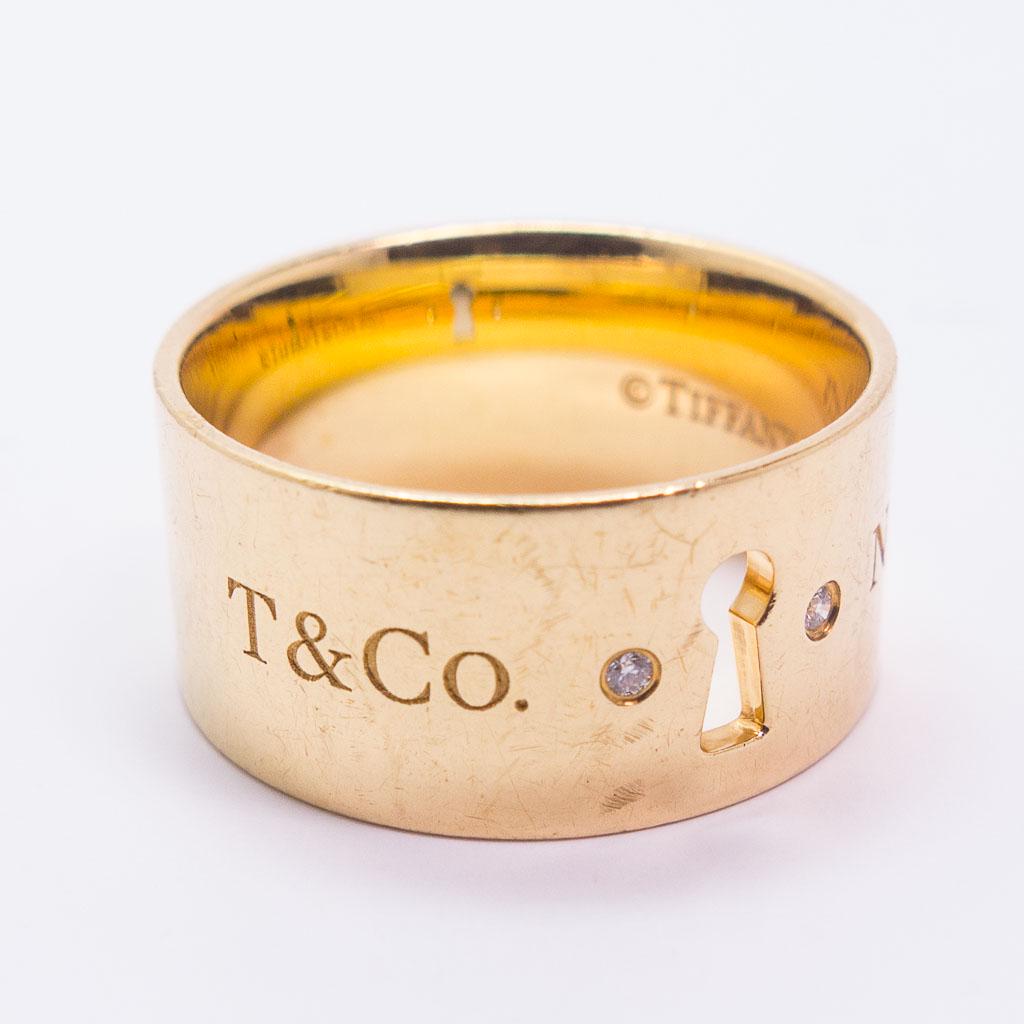 18K Gold Tiffany & Co Keyhole Diamond Ring Band Size 7: This Tiffany & Co. keyhole band in 18K yellow gold features two round diamond accents. Accompanied by a Tiffany jewelry box. This ring is a size 7, the band is 9.5mm wide and it has two round diamond 