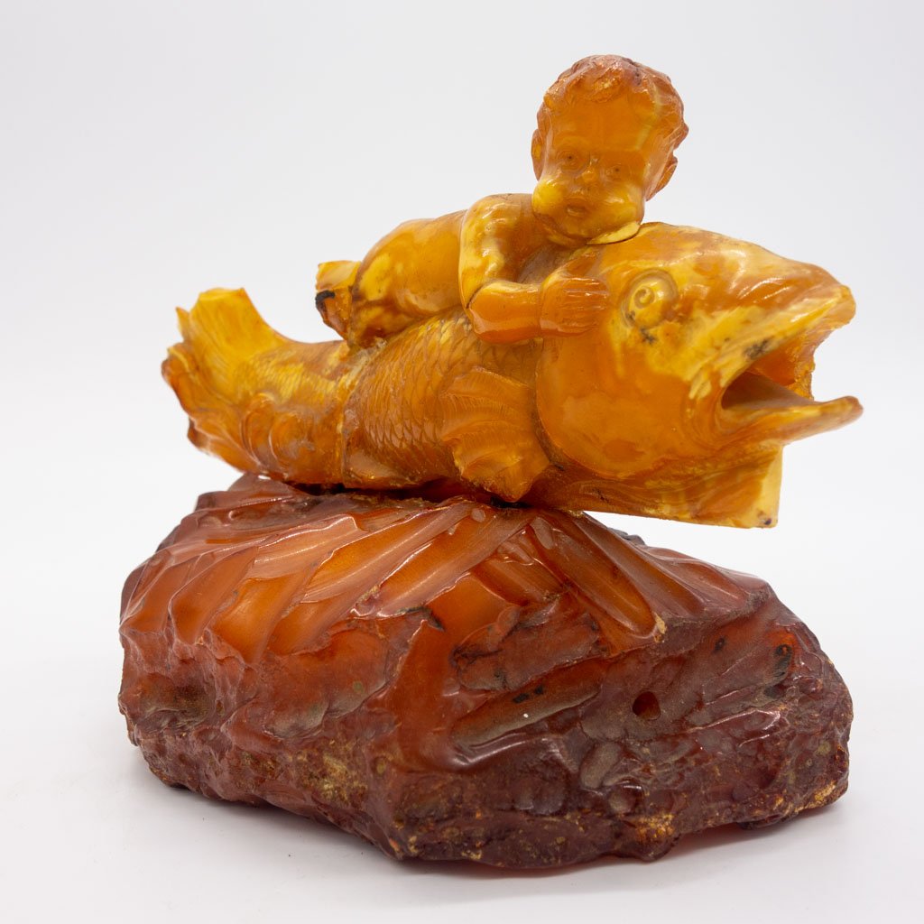 Baltic Egg Yolk Butterscotch Amber Eros on Fish Carving: This is an antique carved Baltic egg yolk and butterscotch amber figurine depicting the Greek god Eros riding a fish. 5 1/2" long x 4 1/4" across x 4 1/2" tall. It weighs a total of 280 ct.