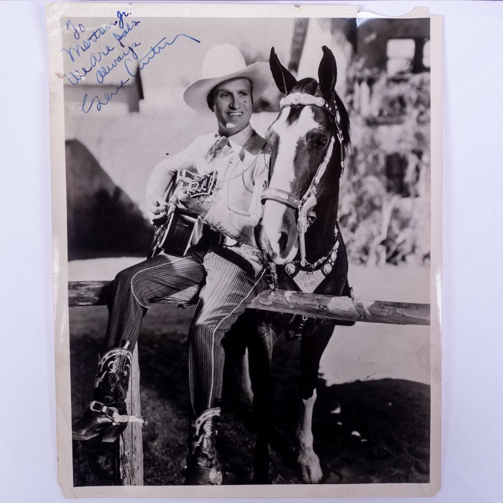 Autograph Signed Photograph of Gene Autry on Fence: An autographed photo of American singer Gene Autry sitting on a fence with his horse and guitar. We guarantee the authenticity of all autographs for the lifetime of the buyer. 10 x 8"