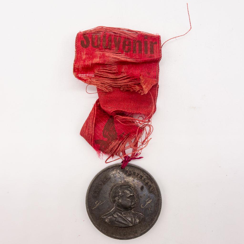 Grover Cleveland 1885 Presidential Campaign Medal: This Presidential campaign medal depicts the side profile of Grover Cleveland on one side and the Washington Monument on the other. It is dated 1885 and hangs from a red souvenir ribbon. 1 3/8"