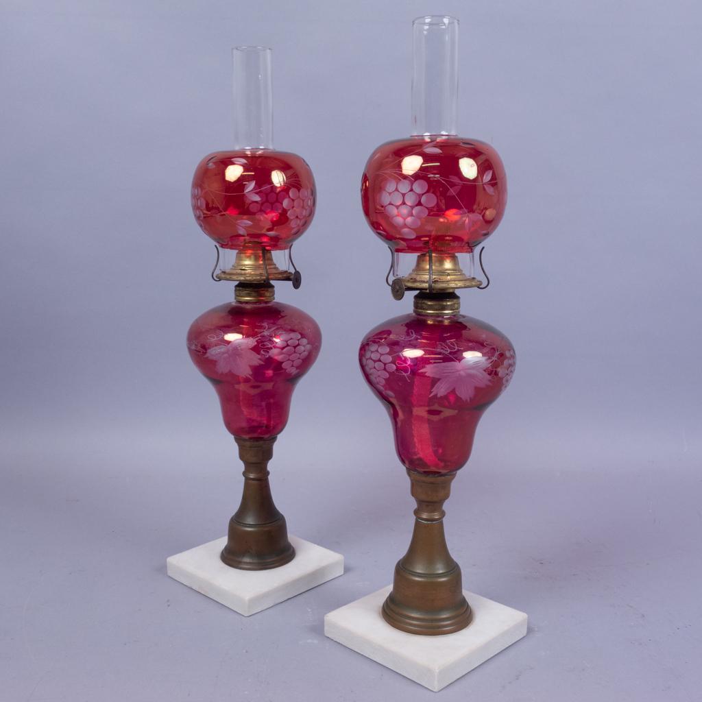 Antique Pair Etched Cranberry Glass Kerosene Lamps: This is an antique pair of cranberry glass kerosene lamps dating to the 19th century. The glass is etched with ornate grape vine and bunch motif. The globes have unusual narrow neck chimneys. 18-18 1/