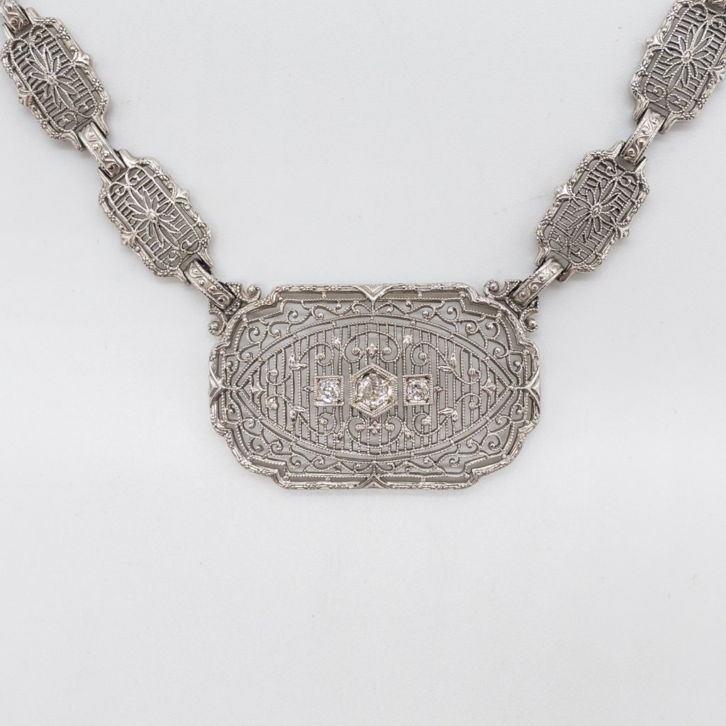 Art Deco 14K White Gold Filigree Diamond Necklace: This is an uncommon antique necklace dating to the 1920s. Rendered in fine 14K white gold, this Art Deco necklace features delicate filigree details and three full cut diamonds at the center. Diamond 