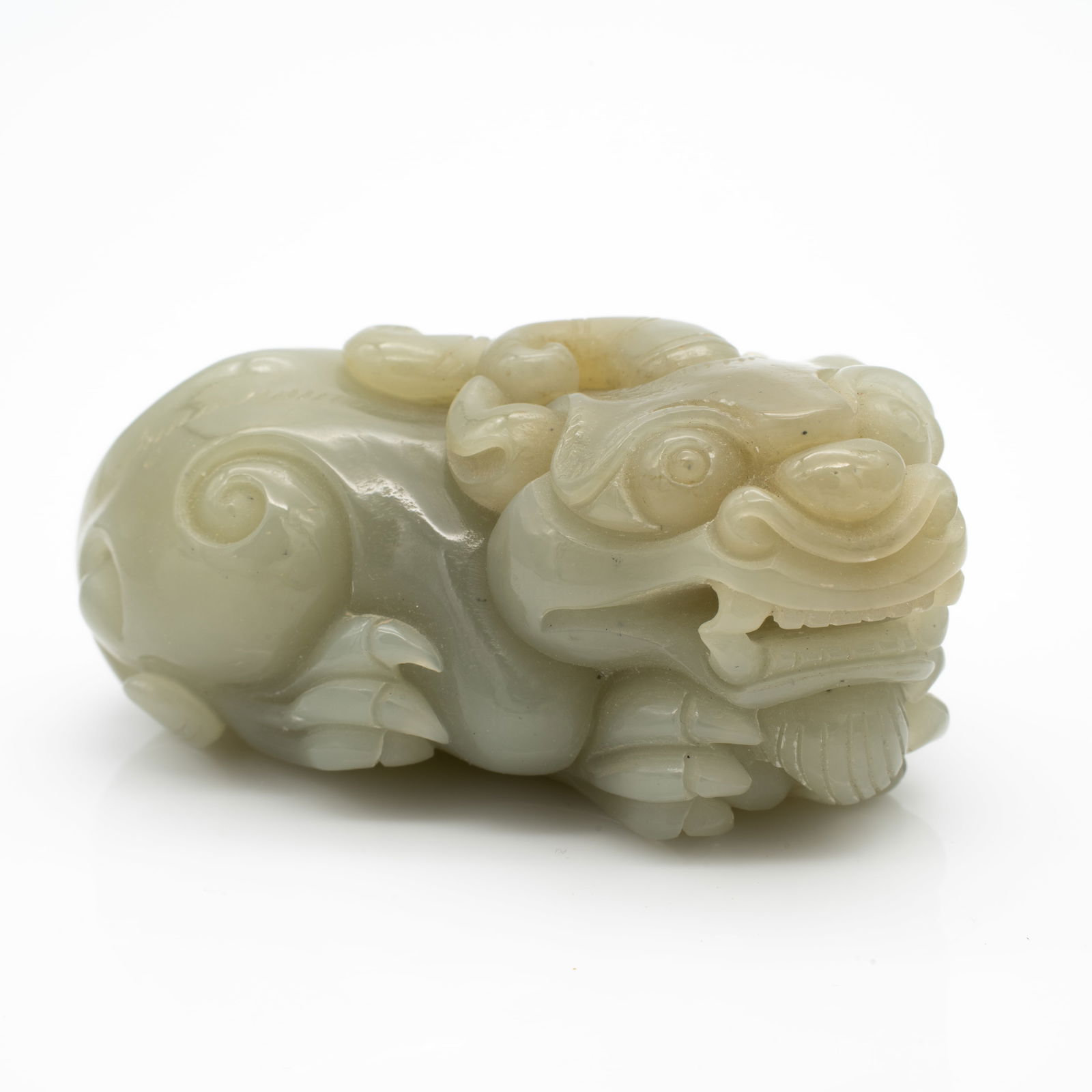 A Carved Chinese Celadon Hardstone Figure of a Recumbent Mythical Beast: Lot 80 A Carved Chinese Celadon Hardstone Figure of a Recumbent Mythical Beast Description: carved from a pale celadon jade with soft translucency and a smooth polish, this piece represents a stylized