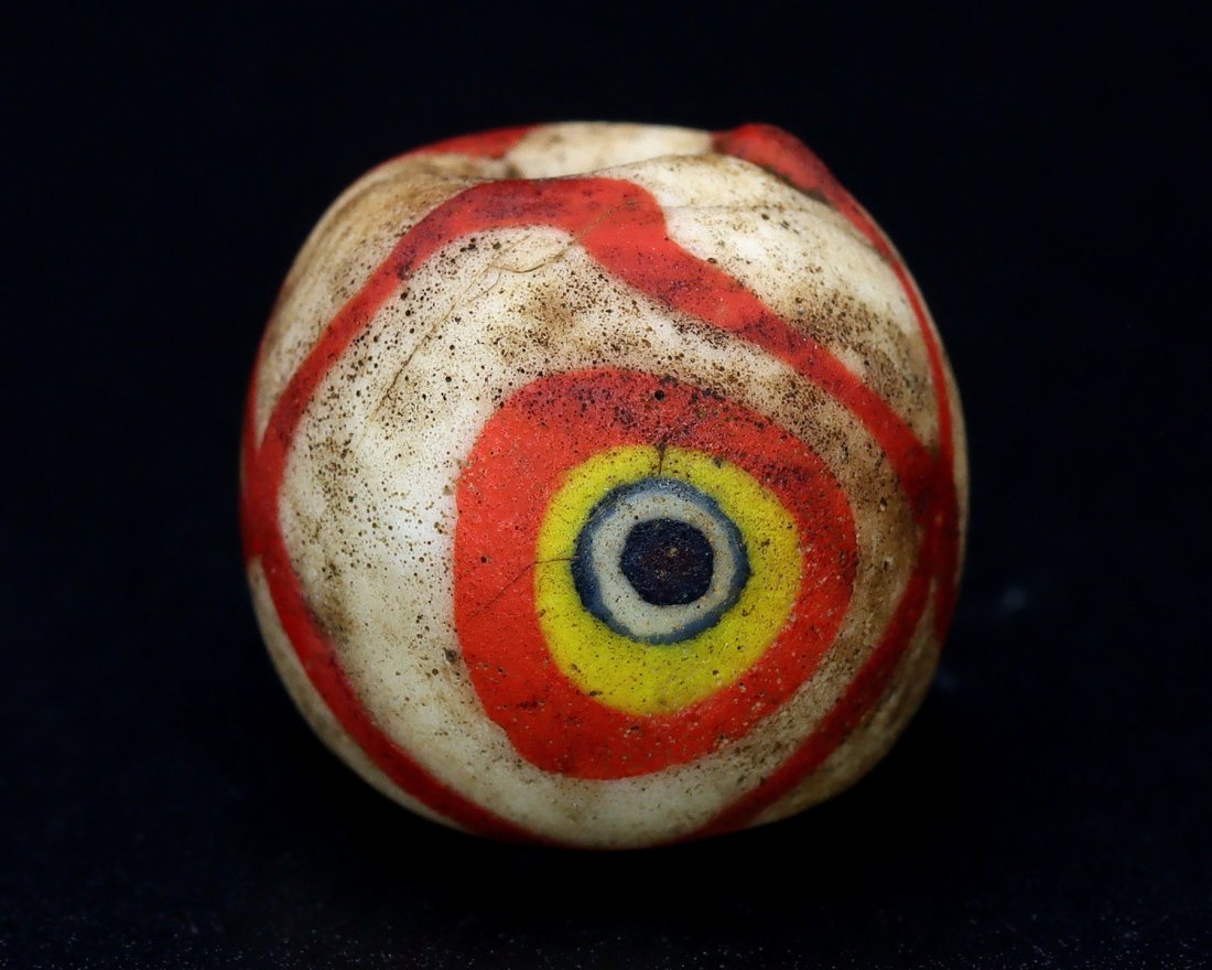 Collection of Ancient Roman Eye Glass Bead by Mr. Omar Zayd: An Ancient Roman Glass Bead Cultures/Periods: 1st-3rd Century AD Dimension: 53/64 x 3/4 inches (21x19x17mm) Findspot: Unknown Provenance: Private Collection, Family in Dubai, acquired in the 2002 from
