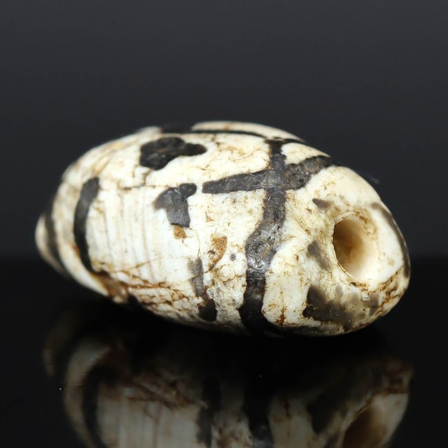 Ancient Etched Agate Dzi Bead from the Maurya Empire (322-185 BC): Dimension: 15x9x6 mm Introduction: Discover a remarkable piece of Indian history with this ancient etched agate Dzi bead from the Maurya Empire, an era marked by significant cultural and political dev