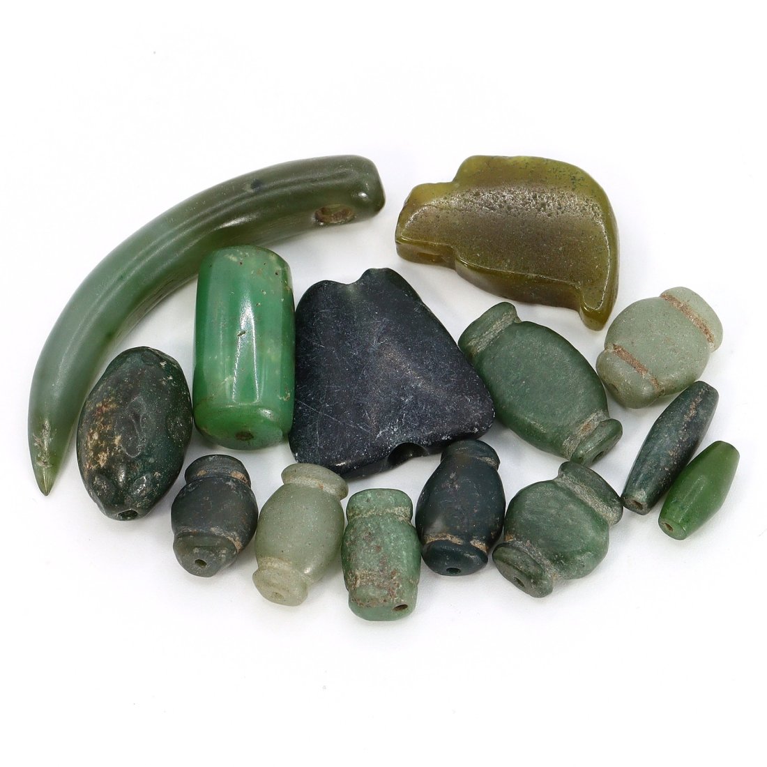 Group of 14 Shang to Ming Dynasty Celadon & Buff Jade Amulets (1600 BC - 1644 AD): This lot presents a selection of 14 Chinese jade amulets, ranging in size from 11-46mm, spanning an extensive period from the Shang Dynasty through to the Ming Dynasty. The collection includes a tusk 