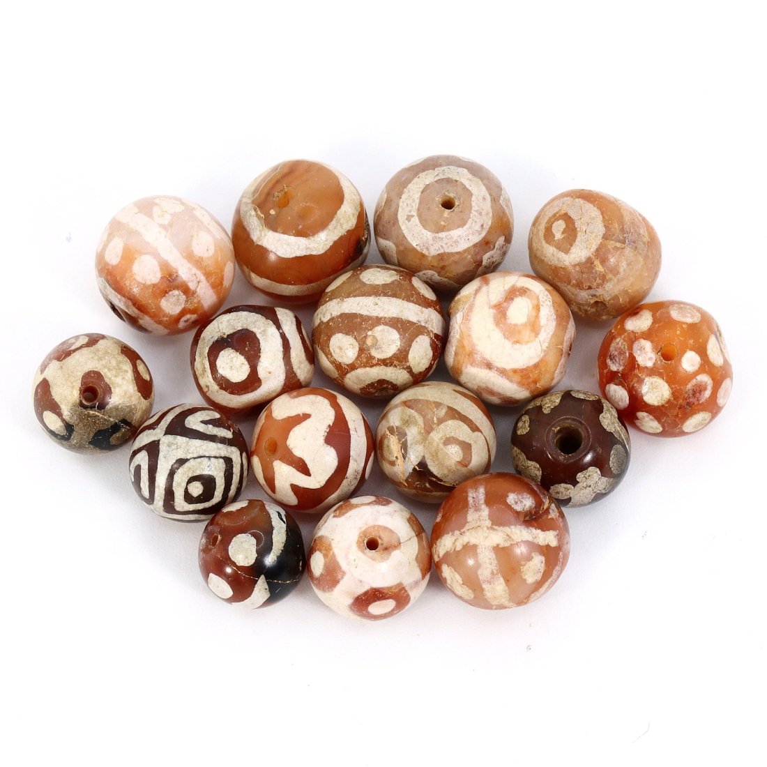 Group of 16 Medieval Himalayan Silk Road Tibetan Etched Carnelian Dzi Beads (6th-17th Century AD): These 16 remarkable Tibetan etched carnelian dzi beads are a testament to the rich history of the Himalayan Silk Road during the Medieval era (6th-17th Century AD). Ranging in dimension from 7mm to 10