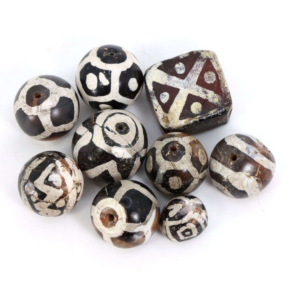 Group of 9 Ancient Tibetan Etched Black Carnelian Dzi Beads (Medieval Era): These exquisite Tibetan artifacts, a group of 9 ancient etched black carnelian dzi beads, originate from the Himalayan Silk Road during the Medieval era. With dimensions ranging from 7mm to 12mm, thes