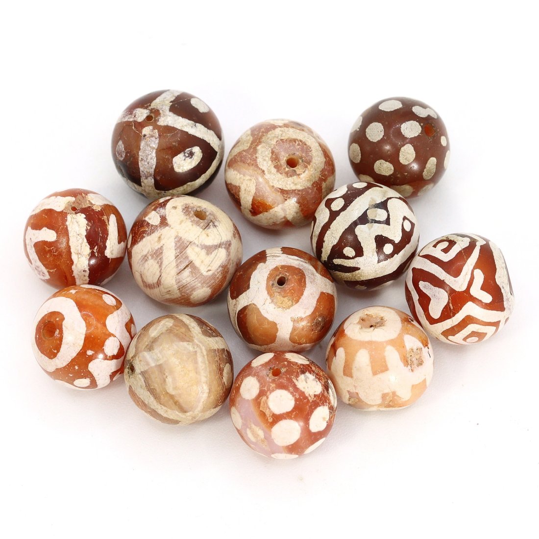 Group of 12 Medieval Himalayan Silk Road Tibetan Etched Carnelian Dzi Beads (6th-17th Century AD): These remarkable Tibetan etched carnelian dzi beads, totaling 12 in number, offer a captivating glimpse into the history of the Himalayan Silk Road during the period spanning from the 6th to the 17th 