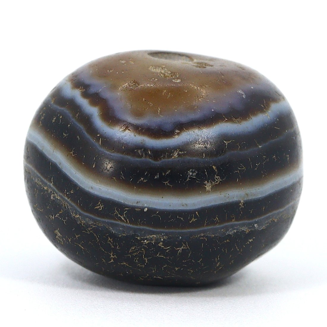 Ancient Tibetan Bhaisajyaguru Dzi Bead, 1st Millennium AD: This bead is a Tibetan Bhaisajyaguru Dzi, a type of bead that is deeply valued in Himalayan culture for its spiritual significance. The bead measures 18x14mm and is made of banded agate, known for its