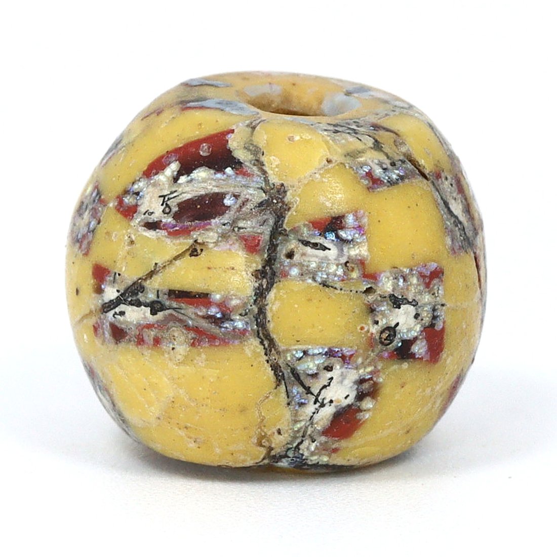 A Roman Period Egyptian Mosaic Glass Bead, 1st Century B.C. - 1st Century A.D.: This mosaic glass bead from the Roman period in Egypt, measuring 1.2 by 1.1 cm, is a dazzling example of ancient craftsmanship. The bead features a yellow base with a pattern of red, white, and blue t