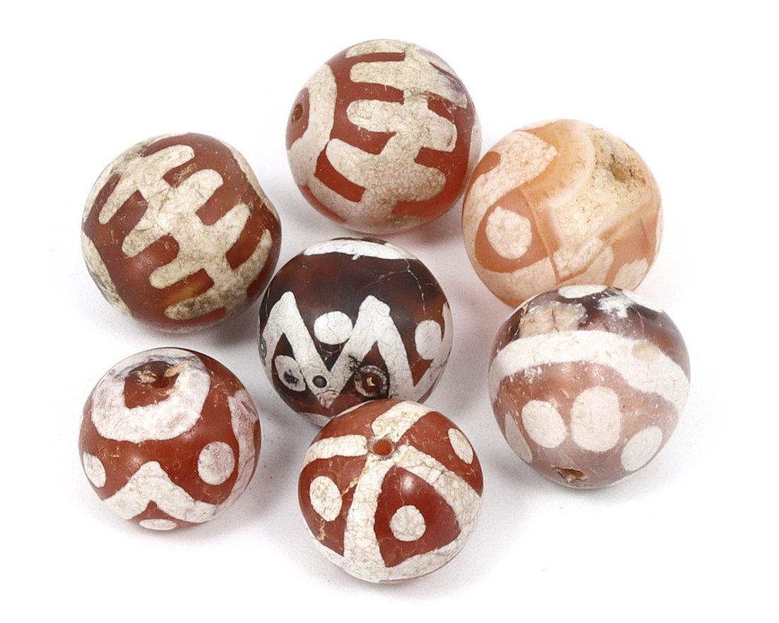 Group of 7 Medieval Himalayan Silk Road Tibetan Etched Carnelian Dzi Beads (6th-17th Century AD): These 7 remarkable Tibetan etched carnelian dzi beads are a testament to the rich history of the Himalayan Silk Road during the Medieval era (6th-17th Century AD). Ranging in dimension from 8mm to 9mm