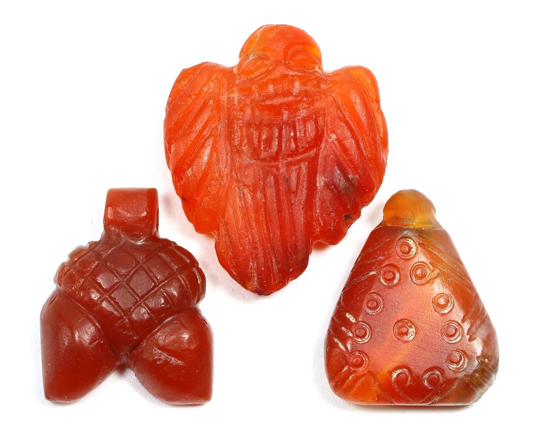 An Ancient Egyptian Collection of Carnelian Amulets: This exquisite trio of carnelian amulets, each measuring around 2.5 cm, hails from the deserts of Ancient Egypt. The warm, translucent orange-red hue of the carnelian, a stone revered for its protecti