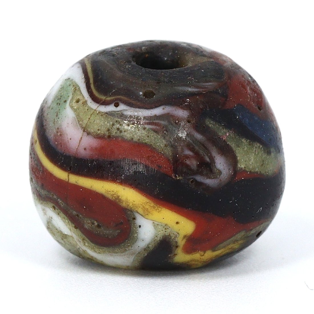 A Multicolored Ancient Egyptian Glass Bead, New Kingdom, 1550-1070 B.C.: Crafted during the New Kingdom period, this exquisite glass bead is a testament to the ingenuity of Ancient Egyptian artisans. With a swirling palette of red, yellow, white, and blue, the bead's intri