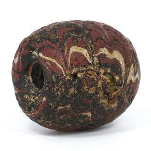 An Egyptian Core-Formed Glass Bead, Embodiment of Alchemy and Artistry: Encapsulating the ancient world's fascination with transformation, this Egyptian core-formed glass bead echoes the sophistication of Late Period artisans. Swirling with deep reds and ochres