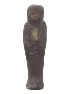 An Egyptian Steatite Ushabti: A Vestige of Ritual and Remembrance: Shrouded in the patina of millennia, this elongated ushabti, crafted from the earthy steatite, stands 15 cm tall as a solemn memento from the Egyptian epoch. Its surface bears the faded vestiges of pa