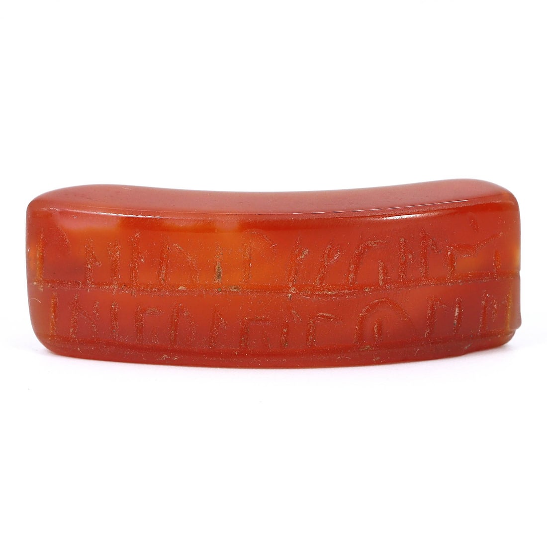 A Vintage Incised Carnelian Bead, 20th Century: This modern carnelian bead, with its polished surface and incised decorative elements, is indicative of 20th-century craftsmanship. The bead's elongated form and curved profile are accented with tradi
