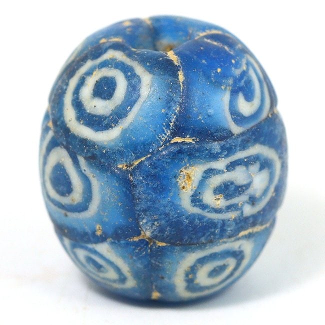 An Ancient Roman-Byzantine Blue Glass Eye Bead, 1st-4th Century CE: This exquisite Roman-Byzantine glass bead exemplifies the period's glasswork mastery, featuring the classic 'evil eye' motif intended to ward off malevolent gazes. The swirling patterns and intense co