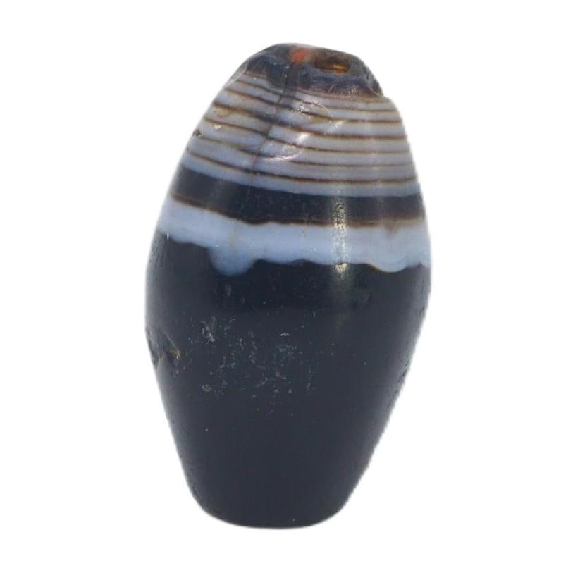 An Ancient Tibetan Banded Agate Chung Dzi Bead, 6th-10th Century AC: This chung dzi bead, with its enigmatic dark hues and stark banding, is a quintessential artifact of Tibetan culture. Dzi beads are deeply rooted in Tibetan tradition, often used as protective amulets