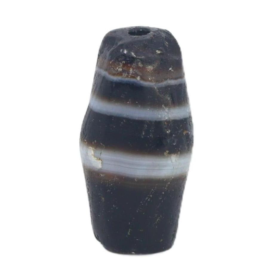 An Ancient Tibetan Banded Agate Chung Dzi Bead, 6th-10th Century AC: This chung dzi bead, with its enigmatic dark hues and stark banding, is a quintessential artifact of Tibetan culture. Dzi beads are deeply rooted in Tibetan tradition, often used as protective amulets