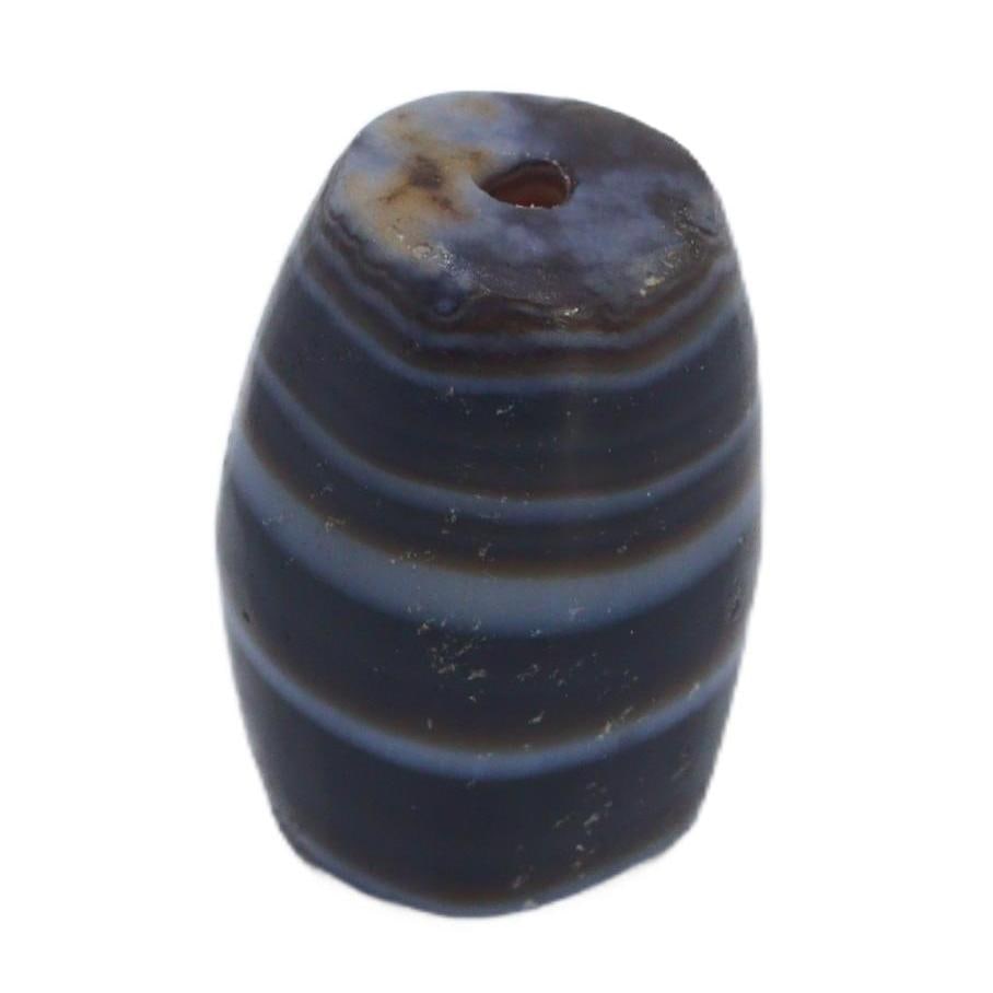 An Ancient Tibetan Banded Agate Chung Dzi Bead, 6th-10th Century AC: This chung dzi bead, with its enigmatic dark hues and stark banding, is a quintessential artifact of Tibetan culture. Dzi beads are deeply rooted in Tibetan tradition, often used as protective amulets