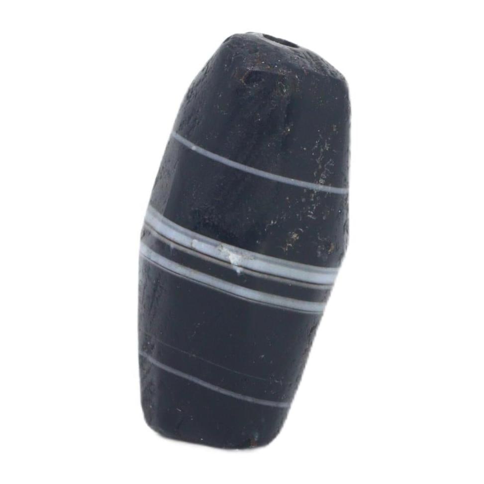An Ancient Tibetan Banded Agate Chung Dzi Bead, 6th-10th Century AC: This chung dzi bead, with its enigmatic dark hues and stark banding, is a quintessential artifact of Tibetan culture. Dzi beads are deeply rooted in Tibetan tradition, often used as protective amulets