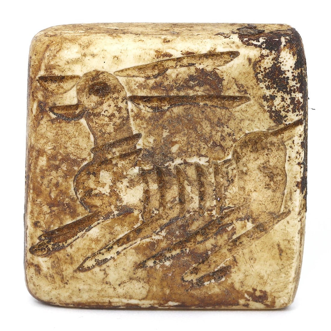 An Ancient Persian Bone Dice with Animal Carving, 1st Millennium BCE: An ancient bone dice from Persia, crafted in the 1st millennium BCE. This bifacial artifact features a carved animal on one face and a three-dot pattern on the other, suggesting its use in ancient gam