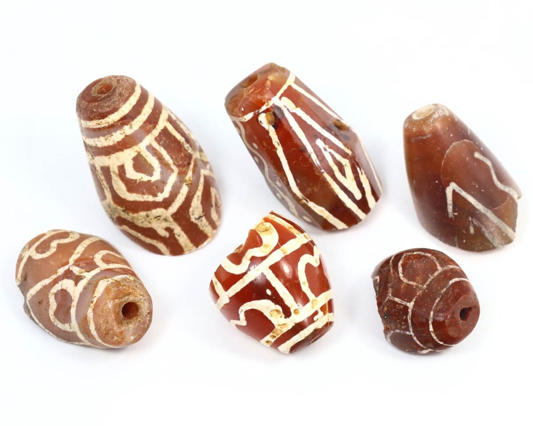 Collection of Tibetan Dzi Beads in Agate and Carnelian, c. 12th - 17th Century: Featuring a collection of agate and carnelian Dzi beads, each piece in this group is adorned with symbolic etchings that hold cultural significance in Tibetan tradition. These ancient beads were highl
