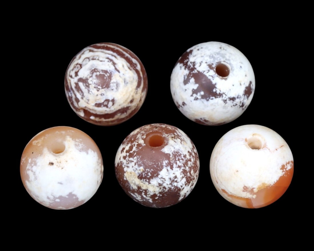 Group of 5 Greco-Bactrian Carnelian Beads, ca. 3rd-2nd Century BCE: A striking ensemble of five Greco-Bactrian carnelian beads, these artifacts date back to the 3rd to 2nd centuries BCE. Exhibiting a range of patterns and hues, from milky white to deep red, each bead 