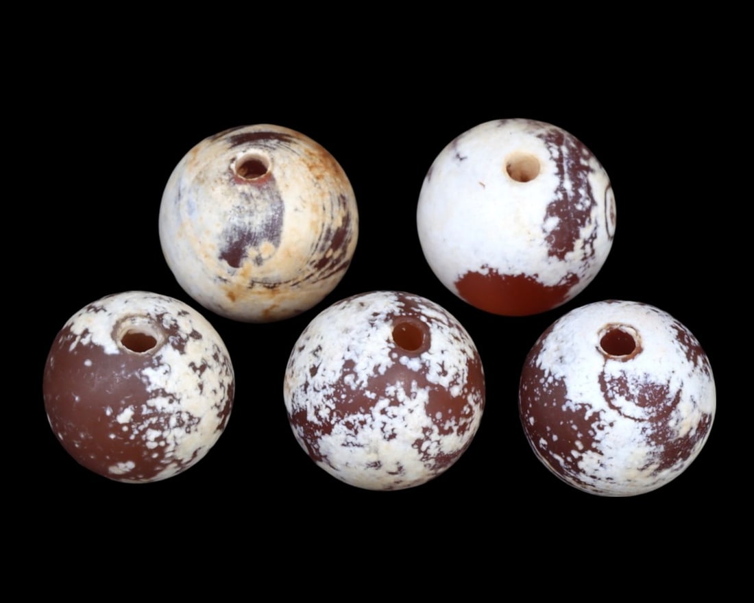 Group of 5 Greco-Bactrian Carnelian Beads, ca. 3rd-2nd Century BCE: A striking ensemble of five Greco-Bactrian carnelian beads, these artifacts date back to the 3rd to 2nd centuries BCE. Exhibiting a range of patterns and hues, from milky white to deep red, each bead 