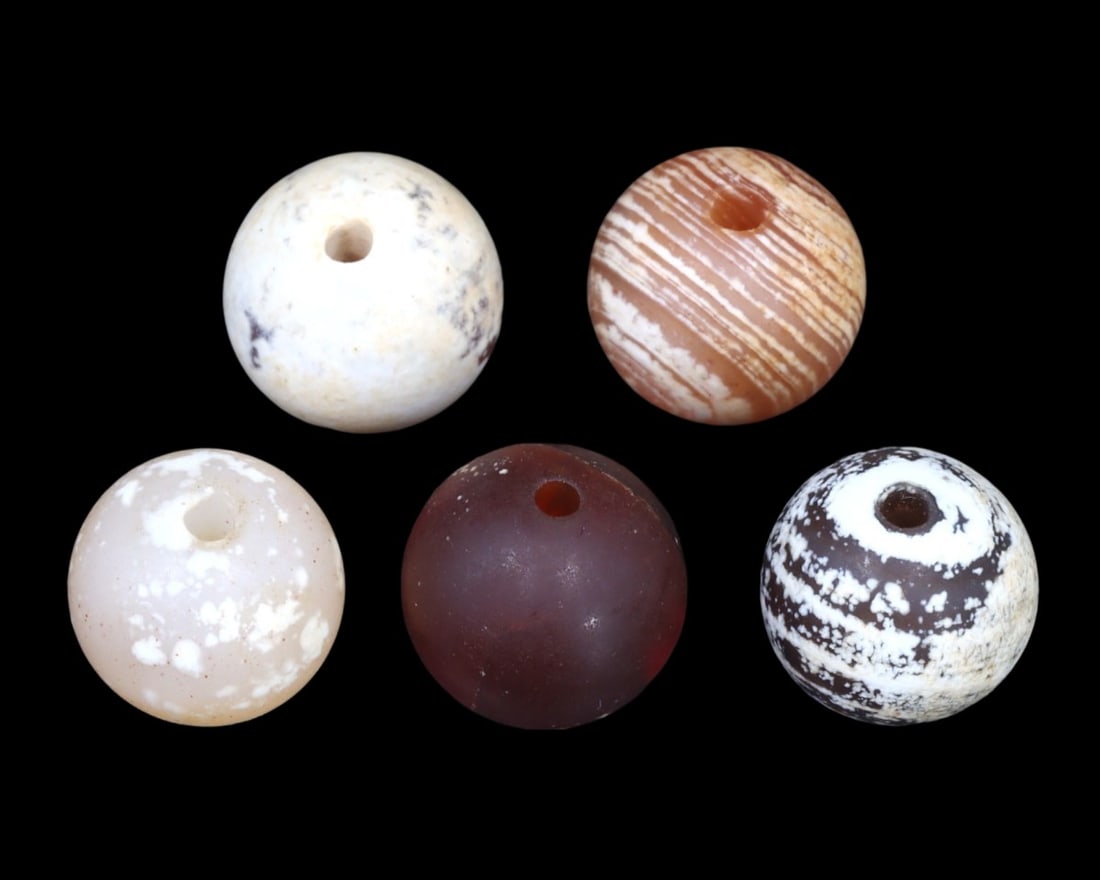 Group of 5 Greco-Bactrian Carnelian Beads, ca. 3rd-2nd Century BCE: A striking ensemble of five Greco-Bactrian carnelian beads, these artifacts date back to the 3rd to 2nd centuries BCE. Exhibiting a range of patterns and hues, from milky white to deep red, each bead 