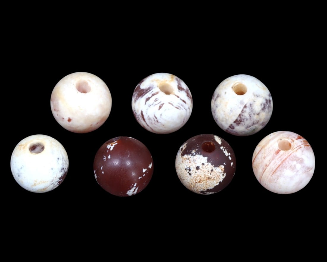 Group of 7 Greco-Bactrian Carnelian Beads, ca. 3rd-2nd Century BCE: A striking ensemble of five Greco-Bactrian carnelian beads, these artifacts date back to the 3rd to 2nd centuries BCE. Exhibiting a range of patterns and hues, from milky white to deep red, each bead 