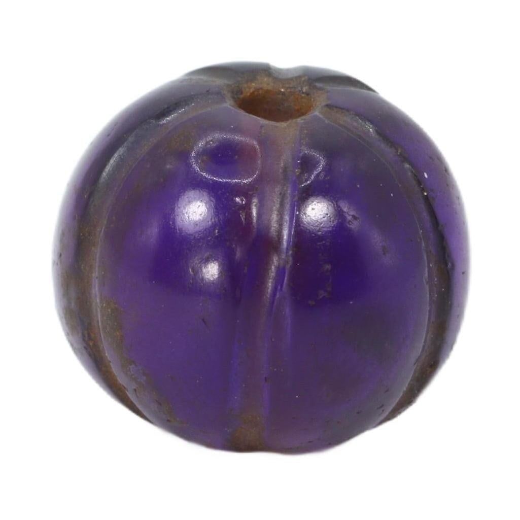 An Antique Mughal Empire Melon-Shaped Amethyst Bead, 16th-19th Century: A distinct South Asian melon-shaped amethyst bead, with a polished surface that accentuates its deep purple hues and natural inclusions. The ribbed melon shape is indicative of the skilled craftsmansh