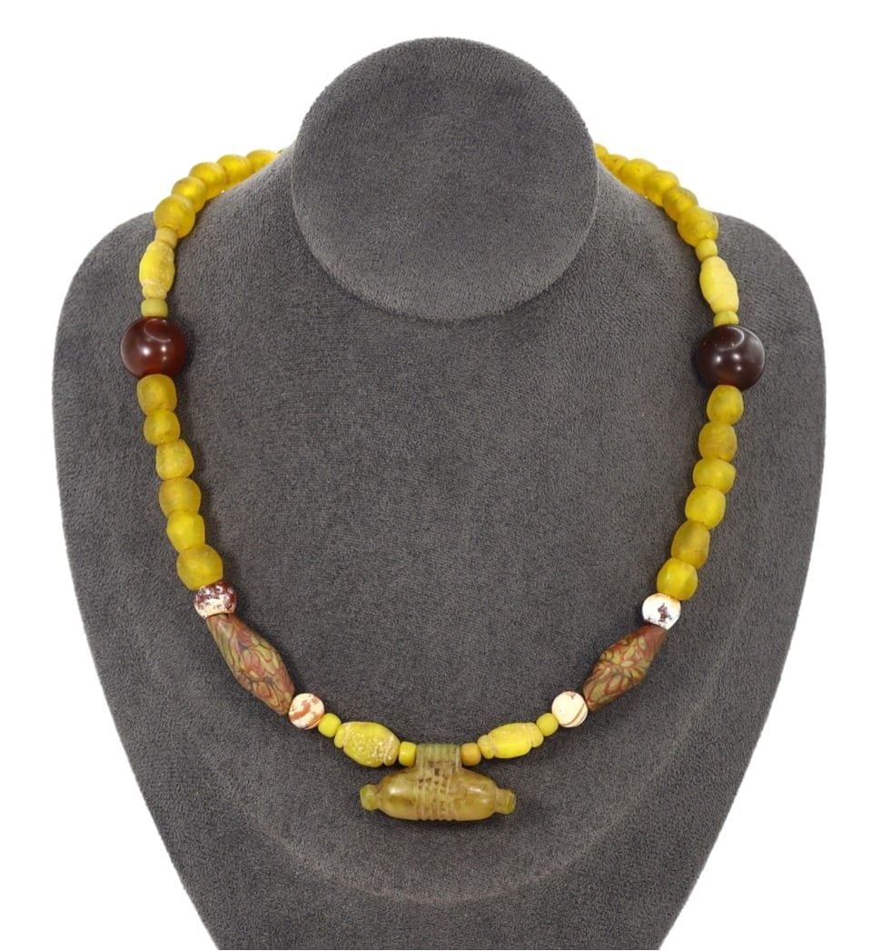 African Tribal West African Glass and Antique Trade Bead Necklace Pendant: This glass and antique trade bead necklace pendant exemplifies the intricate craftsmanship and rich cultural significance of African Tribal beadwork. The centerpiece is a cylindrical bead adorned with