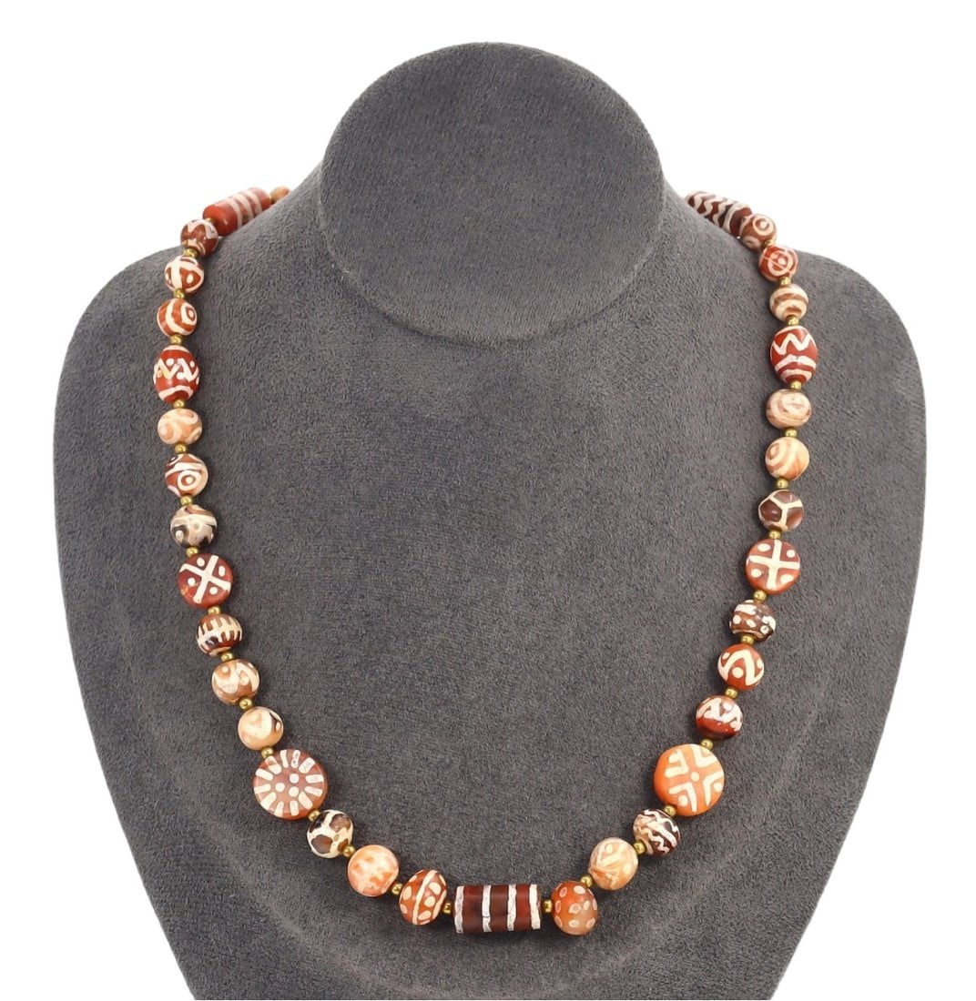 Antique Indo-Himalayan Tibetan Etched Carnelian Beaded Necklace: This etched carnelian beaded necklace exemplifies the exquisite craftsmanship and deep cultural significance of Tibetan artistry. The necklace features a variety of round and cylindrical beads, each a