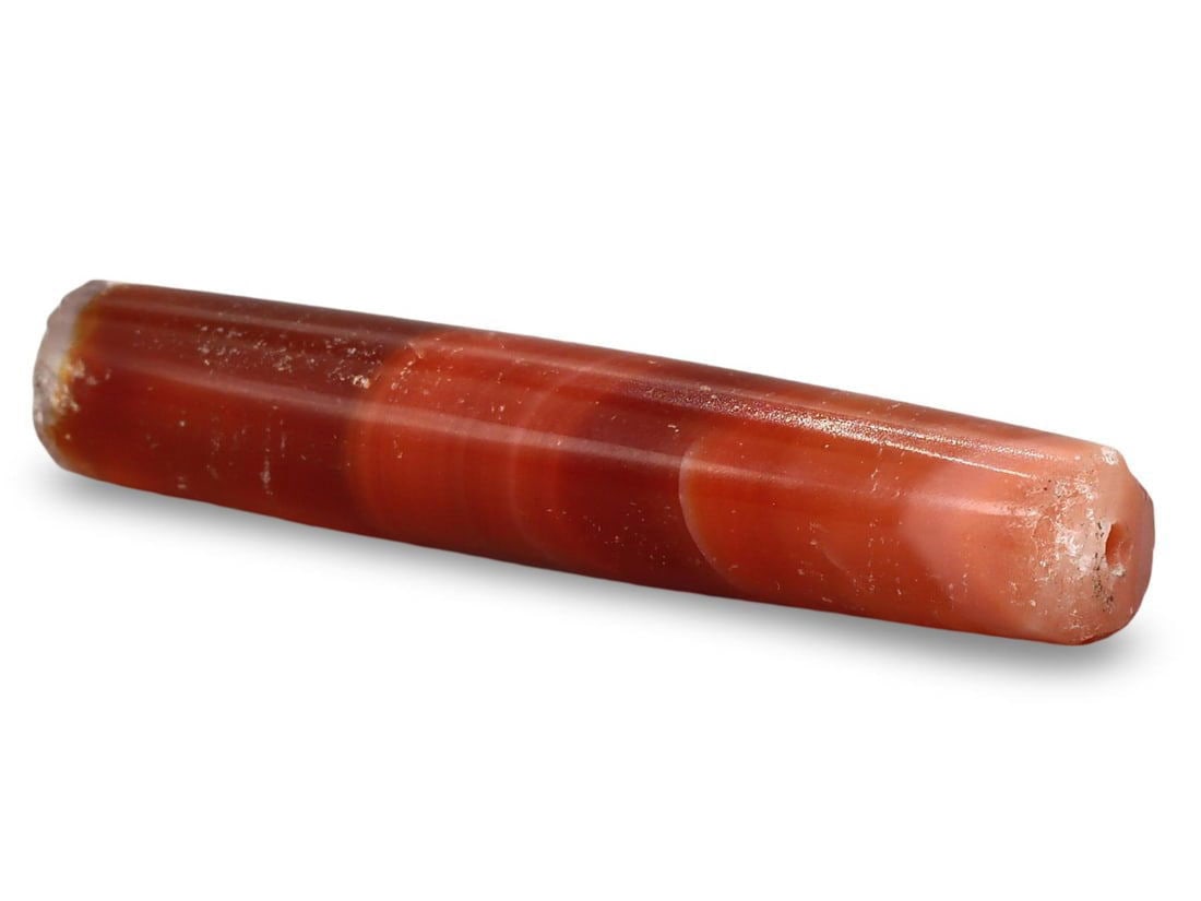 Ancient Late Medieval Sino-Tibetan Carnelian Elongated Bead, 16th-19th Century: This Ancient Late Medieval Sino-Tibetan bead, dating from the 16th-19th century, is an exquisite example of an elongated carnelian bead. The bead features a smooth, polished surface and a rich reddish