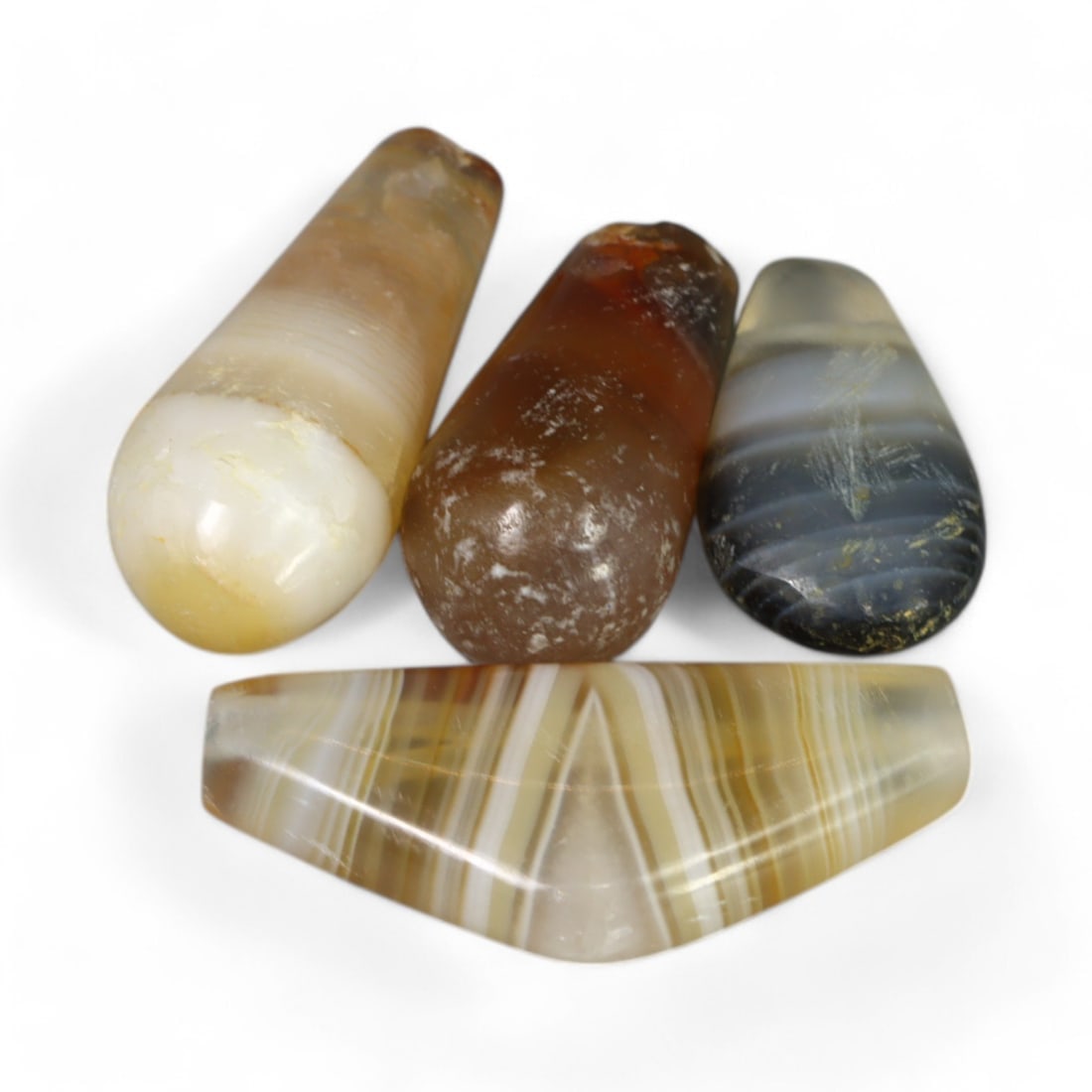 PARTHIAN-ROMAN ERA: Agate Drop Pendants, Circa 1st-3rd Century CE (9g, 25x6mm, 4pcs): This collection of four Parthian-Roman agate drop pendants exhibits an elegant design with natural banding patterns and polished surfaces. The elongated forms and soft, earthy hues of these pendants h